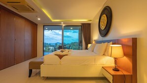 A modern hotel room with a large bed, a bedside table with a lamp, a view of the city, and a large artwork on the wall. - Best Sea View 500m 2 Beach Modern C1 (Rawai)