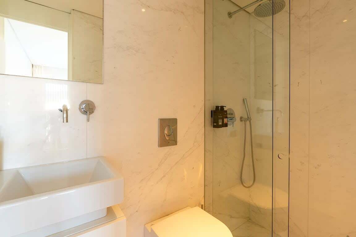 Een badkamer met een wit wastafelmeubel, een spiegel, een douche met glazen deur en een toilet.