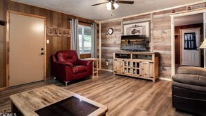 A living room with a red leather chair, a wooden coffee table, a TV stand, and a ceiling fan. - The Lone Pine (Heber-Overgaard)