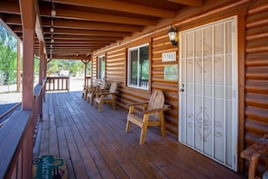Eine Holzhütte mit überdachter Veranda, Nummer 3301, mit einer großen weißen Tür mit dekorativer Metallverzierung und mehreren Holzstühlen, die auf der Veranda angeordnet sind.
