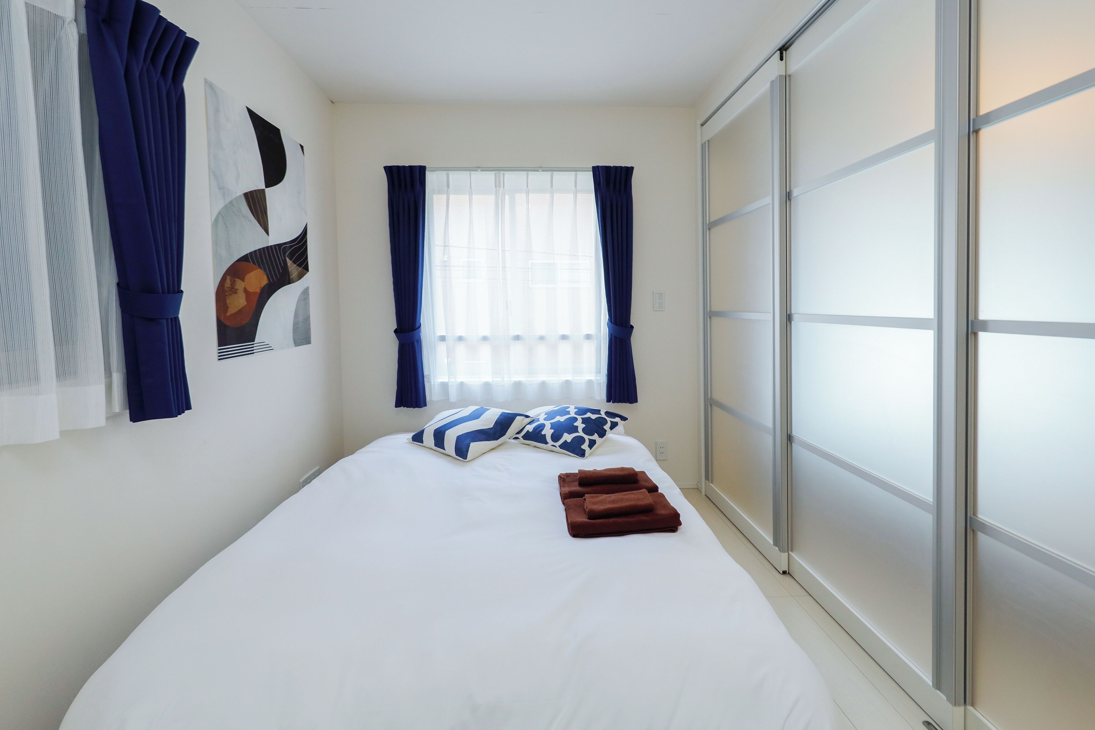 A neatly made bed with pillows, a window with curtains, and a sliding door.