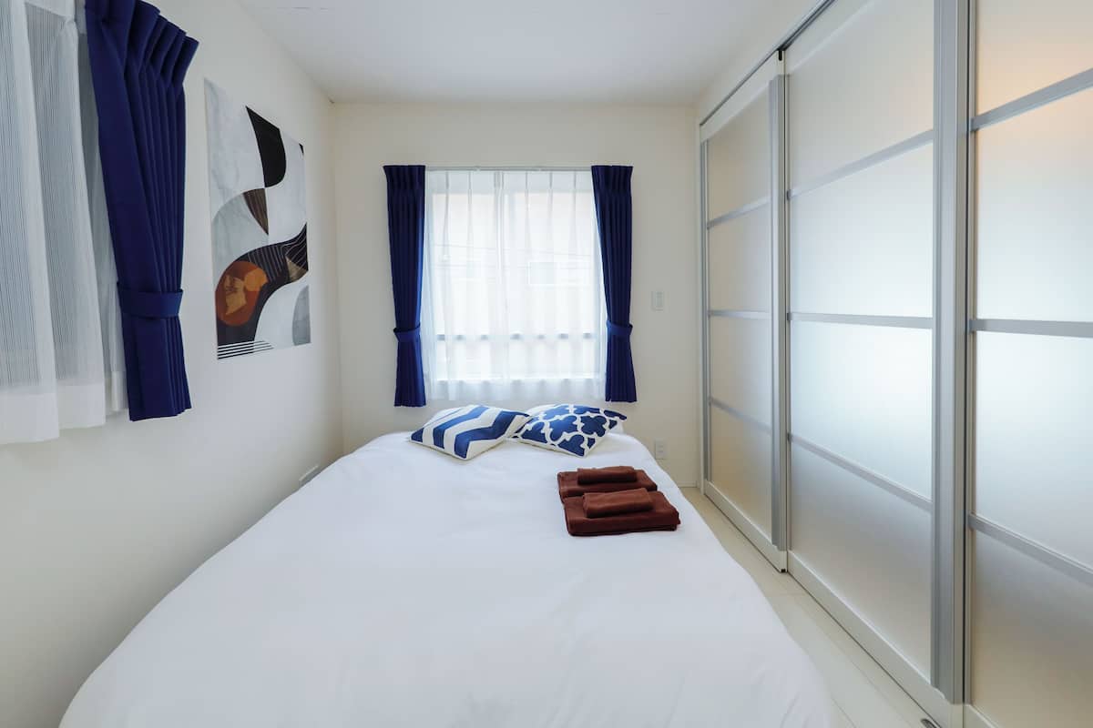 A neatly made bed with pillows, a window with curtains, and a sliding door.
