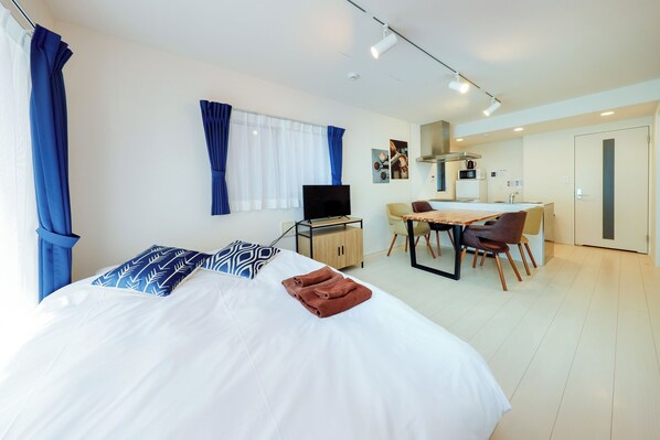 Une chambre d’hôtel équipée d’un lit, d’un bureau, d’une chaise, d’une télévision et d’une kitchenette.