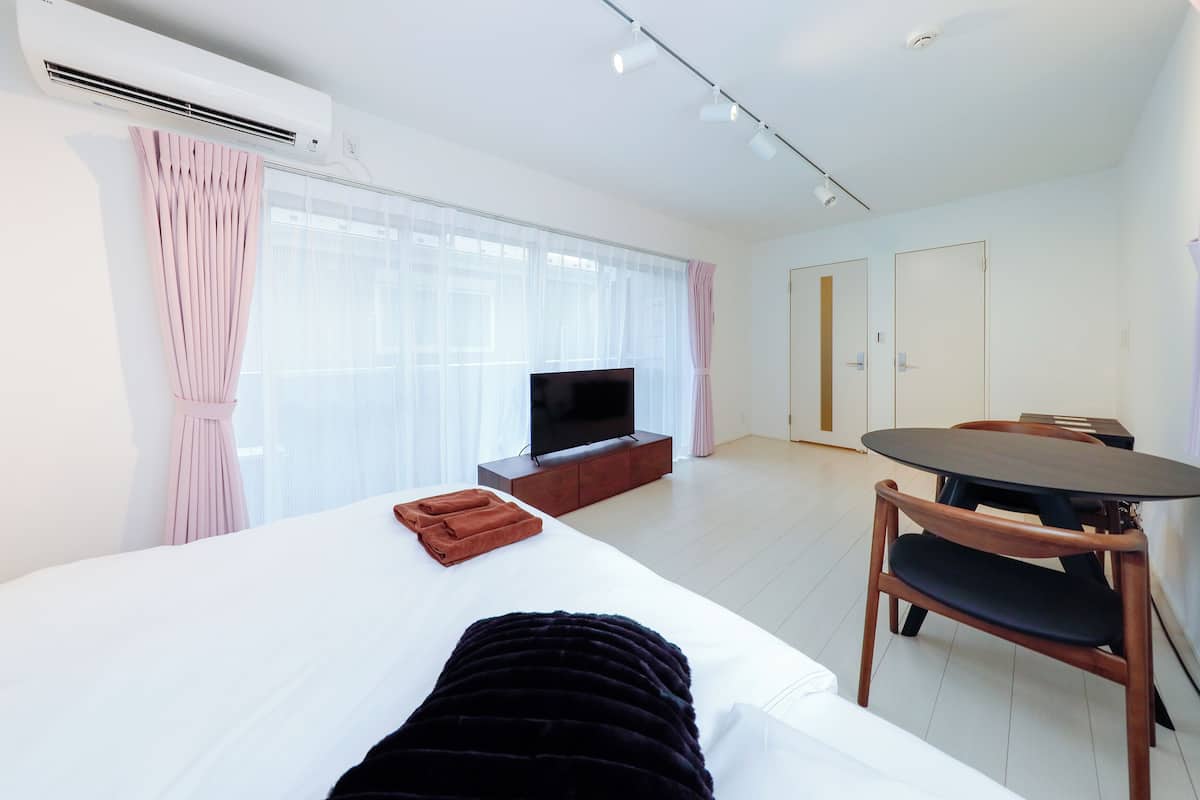 Una habitación de hotel con cama, televisor, mesa de comedor y ventana con cortinas.