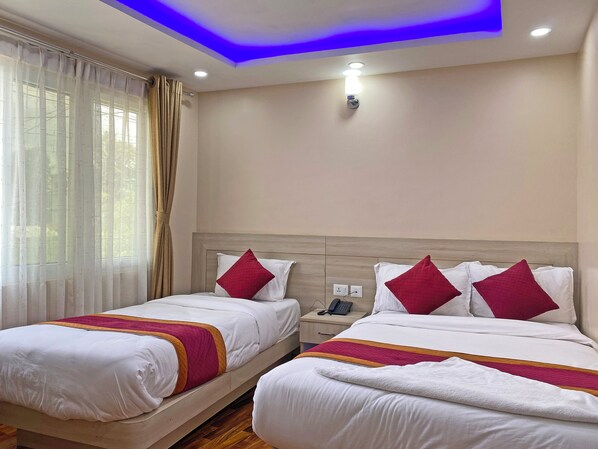 Ein Hotelzimmer mit zwei Betten, jeweils mit weißer Bettwäsche und roten Kissen, einem hölzernen Kopfteil, einem Nachttisch mit Telefon und einem Fenster mit durchsichtigen Vorhängen.
