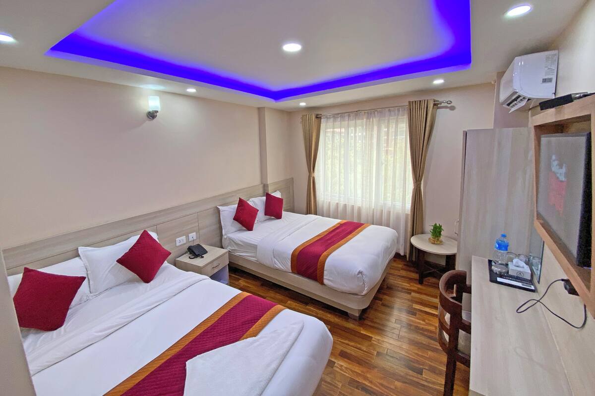 A hotel room with two beds, a desk, a chair, a TV, and a ceiling with blue lighting.