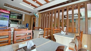 A restaurant interior with wooden furniture, a Coca-Cola refrigerator, and a ceiling fan. - Hotel Aaradhya (Kathmandu)