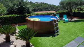 A backyard with a swimming pool, two lounge chairs, and a palm tree.