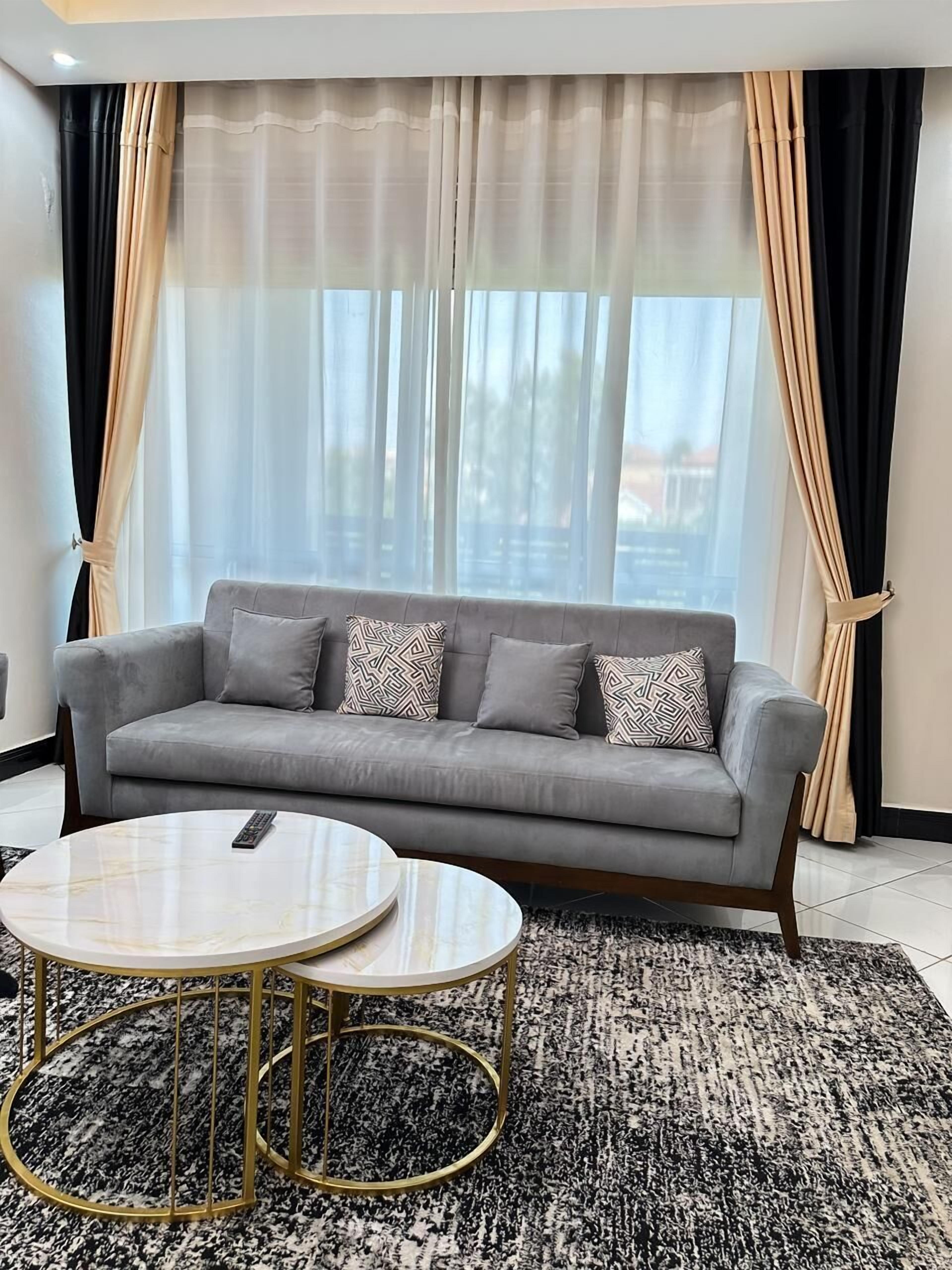 A living room with a grey sofa, patterned cushions, a round coffee table, and a black and white rug.