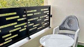 Ein Balkon mit einem weißen Tisch und zwei Stühlen, einer schwarzen Metallabtrennung mit ausgestanzten Mustern und künstlichem Rasenteppich.
