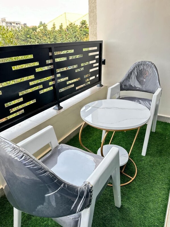 A balcony with a white table and two chairs, a black metal partition with cut-out patterns, and artificial green grass flooring.