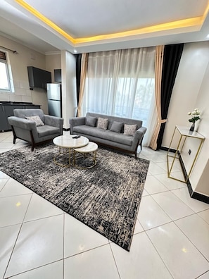 A modern living room with a grey sofa, two armchairs, a coffee table, and a patterned rug.