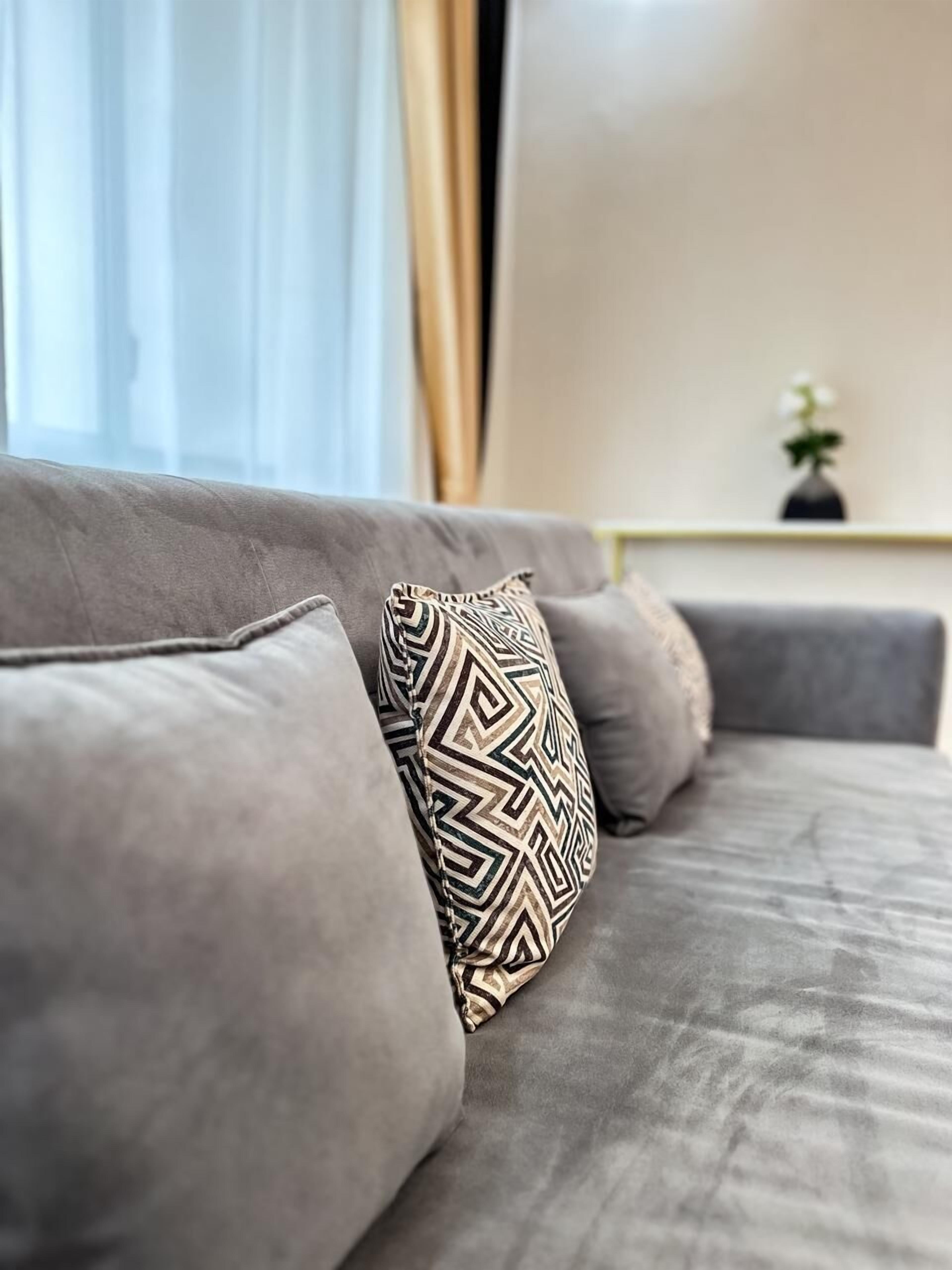 Ein graues Sofa mit gemusterten Kissen und eine Vase mit Pflanze auf einem Beistelltisch.