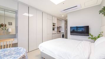 Un dormitorio moderno con una cama grande, un televisor montado en la pared y una kitchenette compacta.