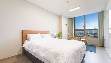 A modern hotel room with a large bed, a small table, and a view of the city through the window.