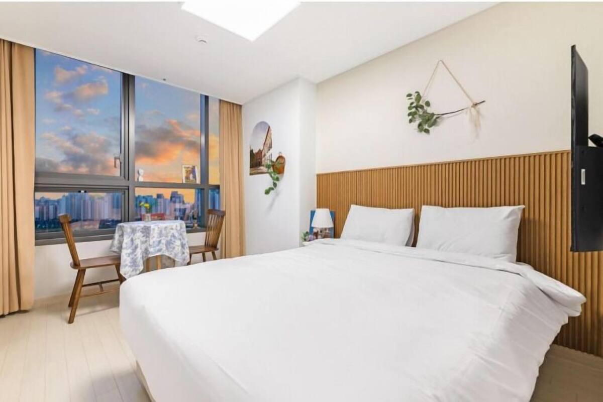 Una camera d'hotel con un letto grande, una scrivania con una sedia, una finestra con vista sulla città e una TV a parete.
