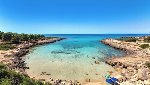 A coastal beach with clear turquoise waters, rocky terrain, and a few umbrellas. - 4076 Villa Baia D'oro by Barbarhouse (Pulsano)