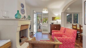 A living room with a fireplace, wicker furniture, and a dining area with wooden chairs and a table. - 4076 Villa Baia D'oro by Barbarhouse (Pulsano)