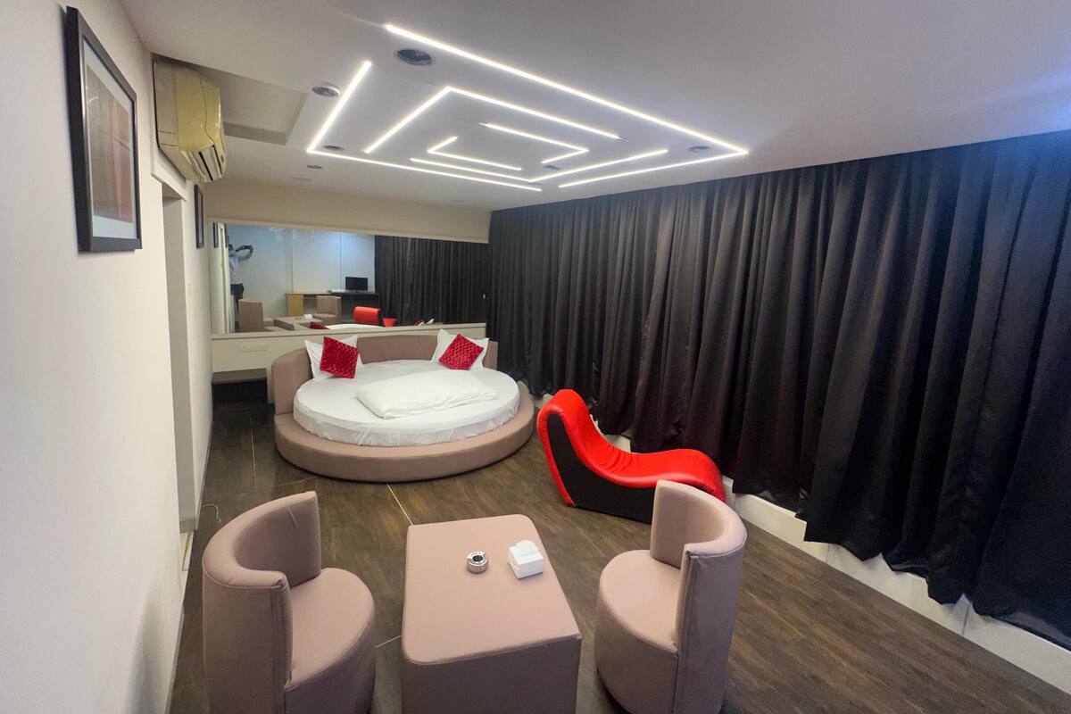 Une chambre d’hôtel moderne avec un lit rond, un fauteuil rouge et une petite table.
