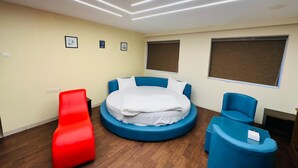 Ein modernes Hotelzimmer mit einem runden Bett, einem roten Sessel, einem blauen Ohrensessel und einem großen Fenster.