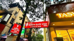 Ein Hotel Eingang mit einem Schild für 'Hotel Aundh Elite Stay' und einem Neonlicht für 'TAS'.