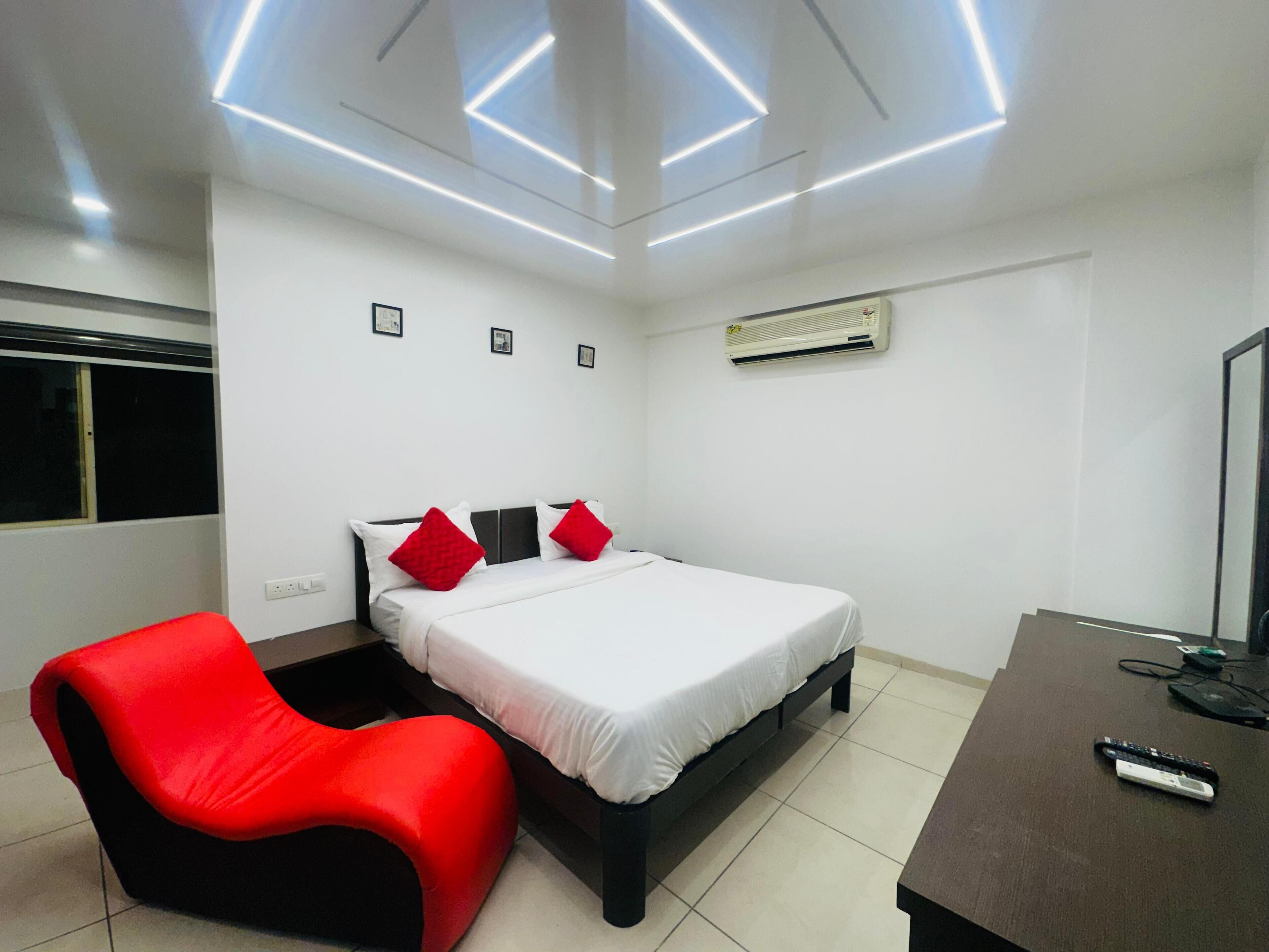 A modern bedroom with a bed, a red chair, a desk, and a ceiling light fixture.