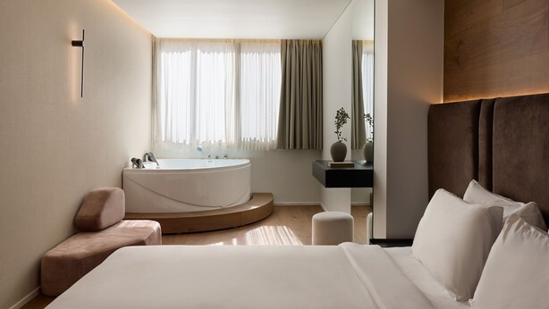 A modern bedroom with a large bed, a round bathtub, and a wooden headboard.