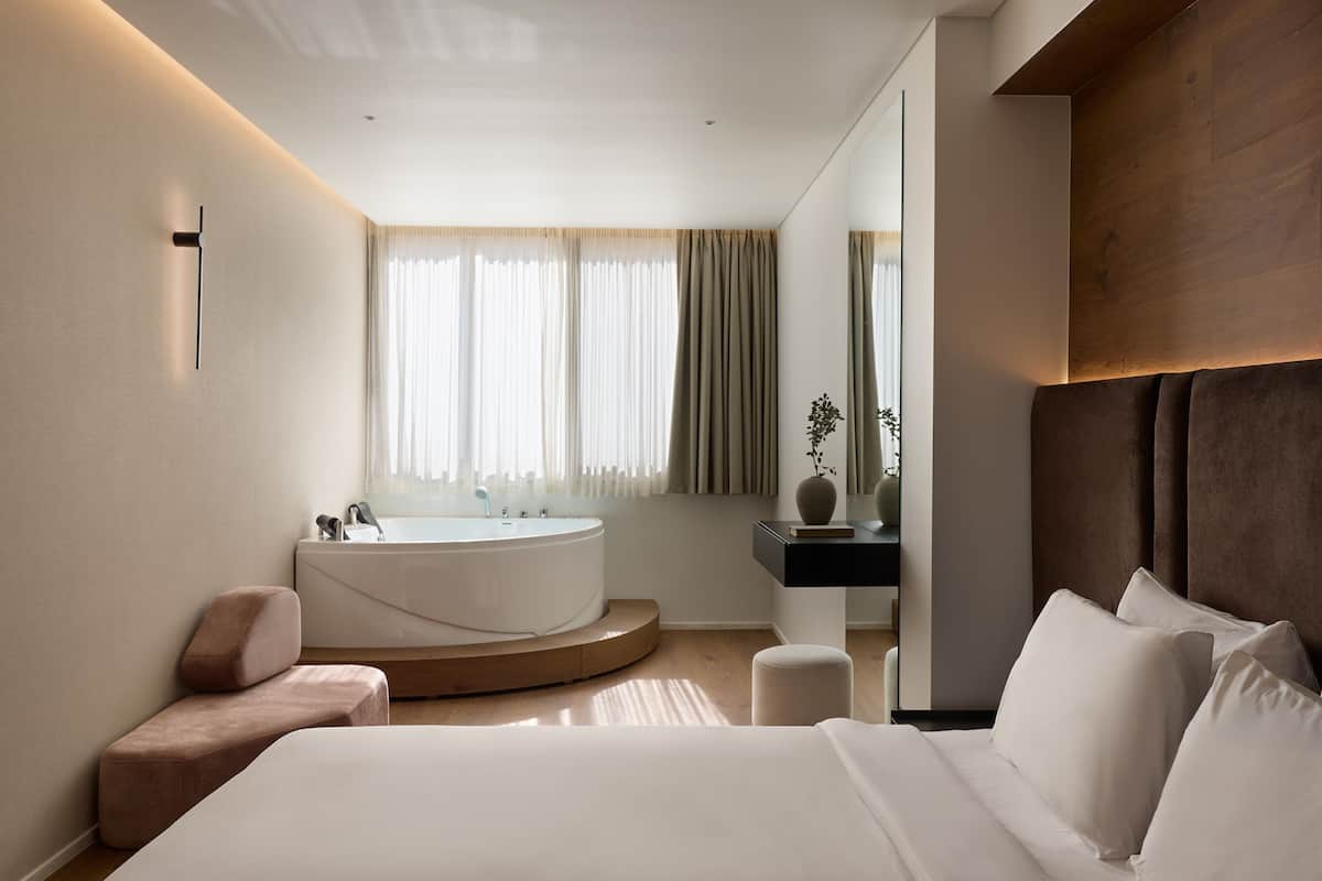 A modern bedroom with a large bed, a round bathtub, and a wooden headboard.