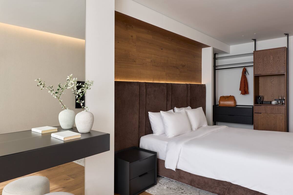 A modern bedroom with a large bed, a bedside table with books, a nightstand, and a wooden headboard.