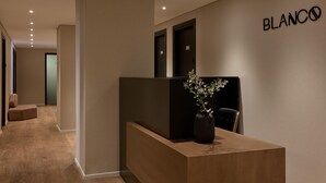 A modern reception area with a wooden reception desk, a potted plant, and a wall-mounted sign that reads "BLANCO".