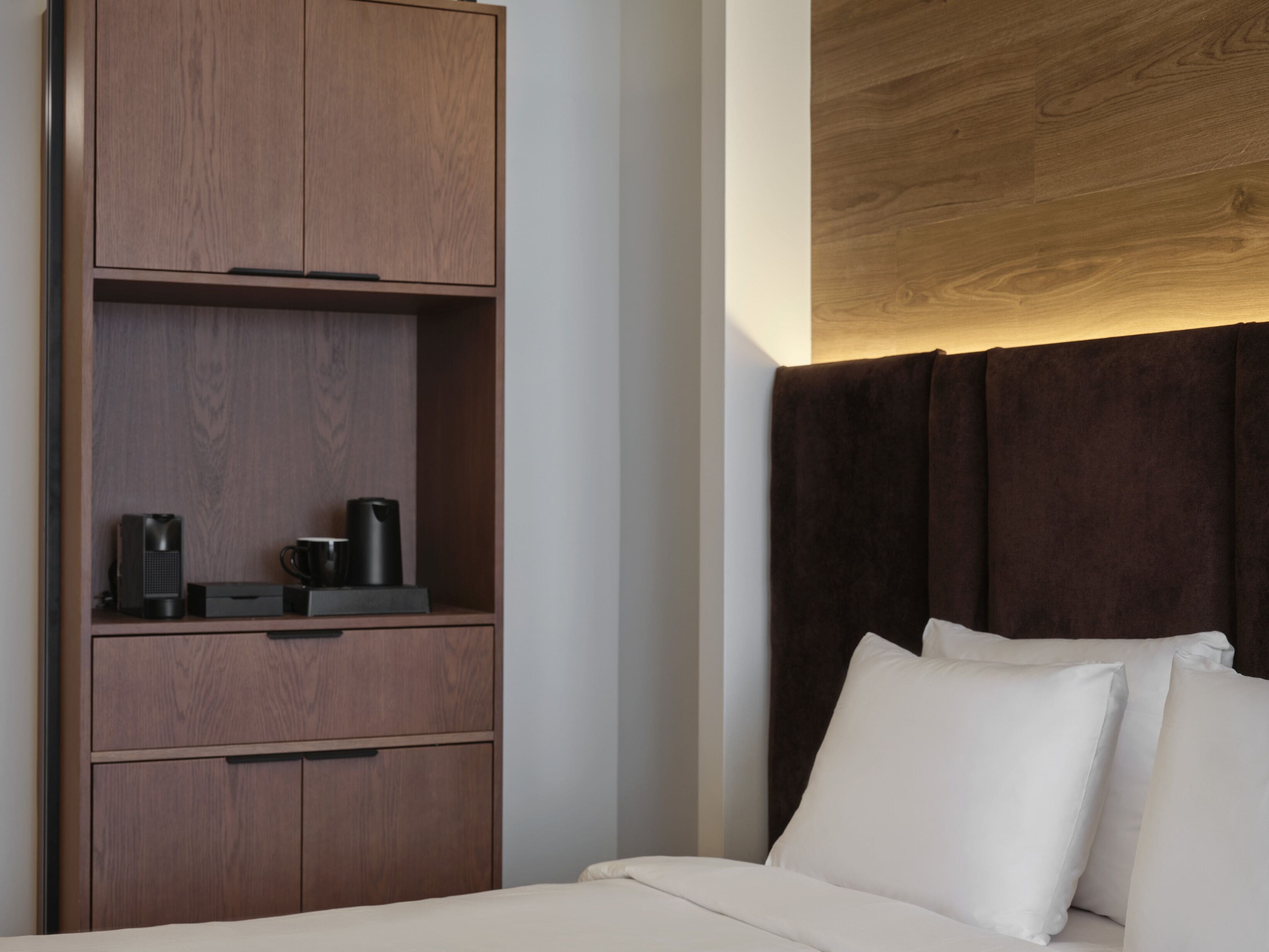 Ein Hotelzimmer mit Holzschrank, Bett mit weißen Leinen und einem dunklen Vorhang.