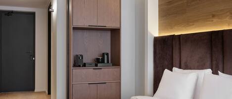 A hotel room with a bed, a wardrobe, a desk, and a dark door.