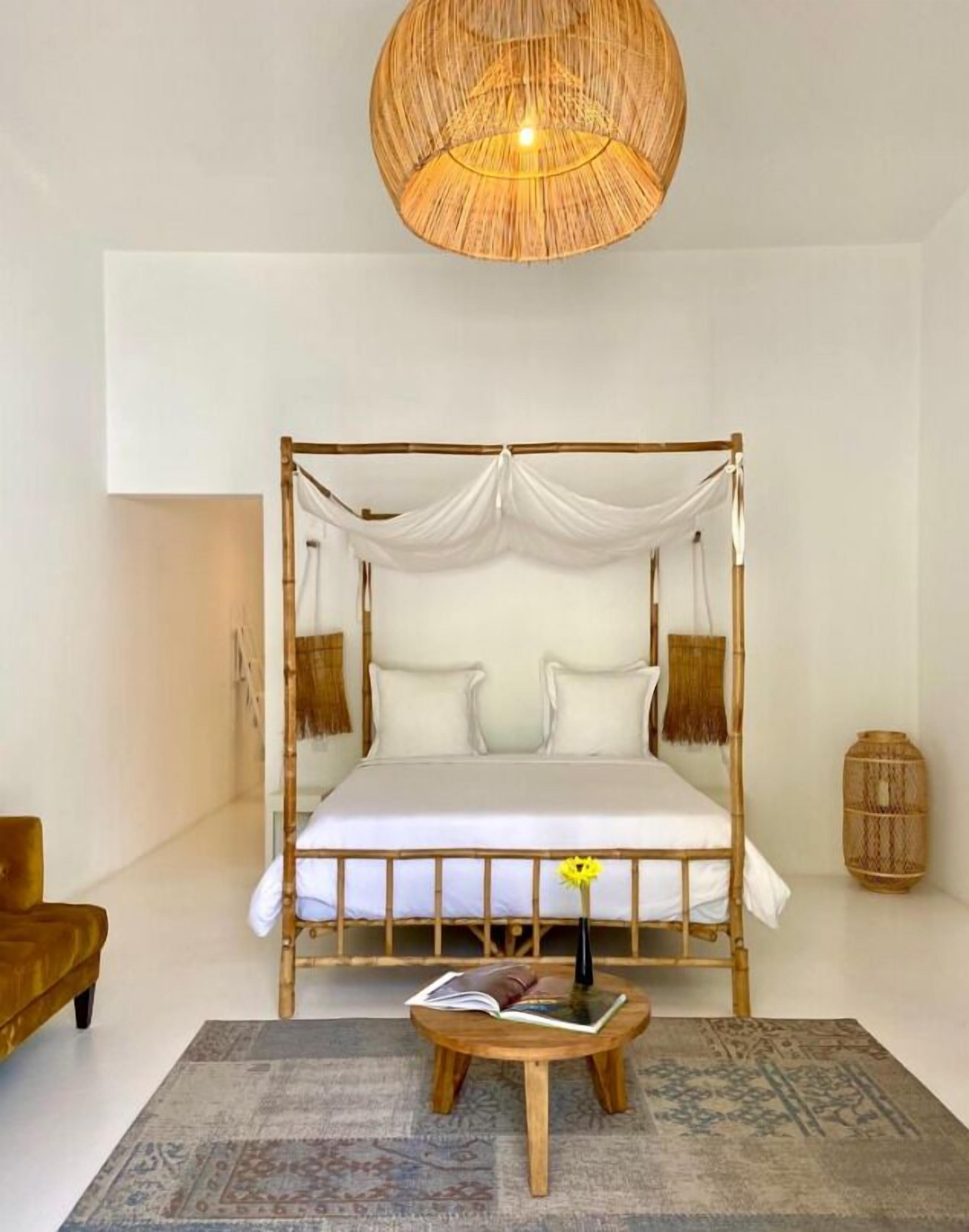 A four-poster bed with white linens, a woven rattan headboard, and a hanging light fixture.