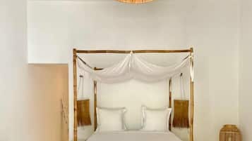 Ein Himmelbett mit weißen Leinen, einem Kopfteil aus gewebtem Rattan und einer Hängelampe.