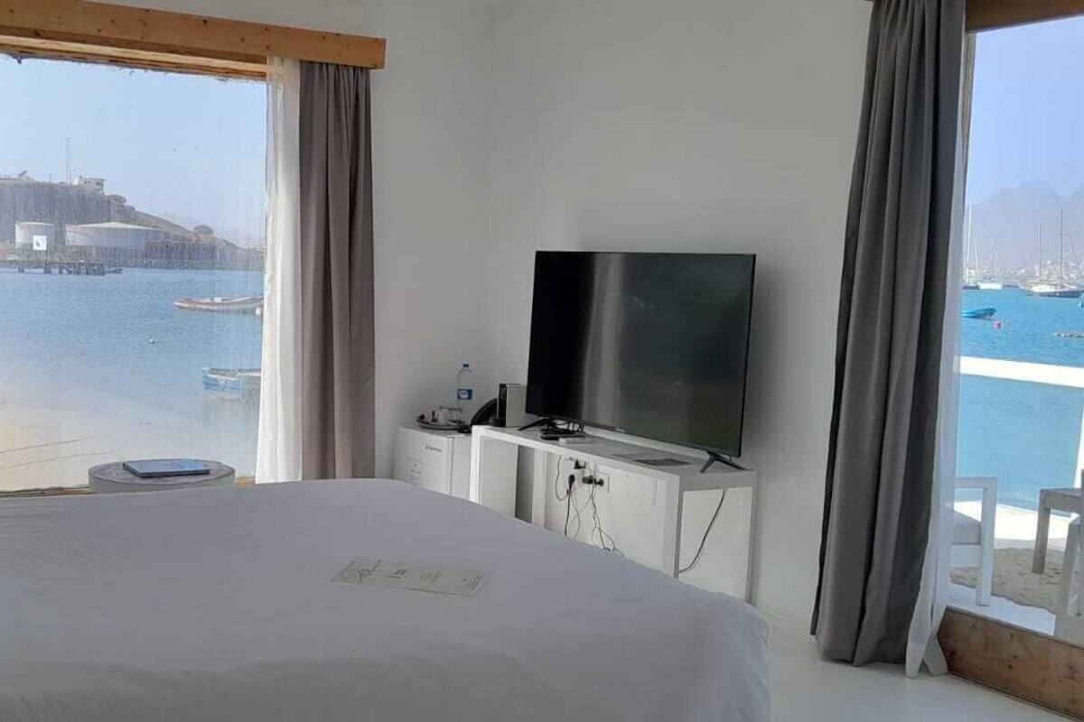 Habitación de hotel con cama, televisión, una mesita y vistas a barcos y un muelle.