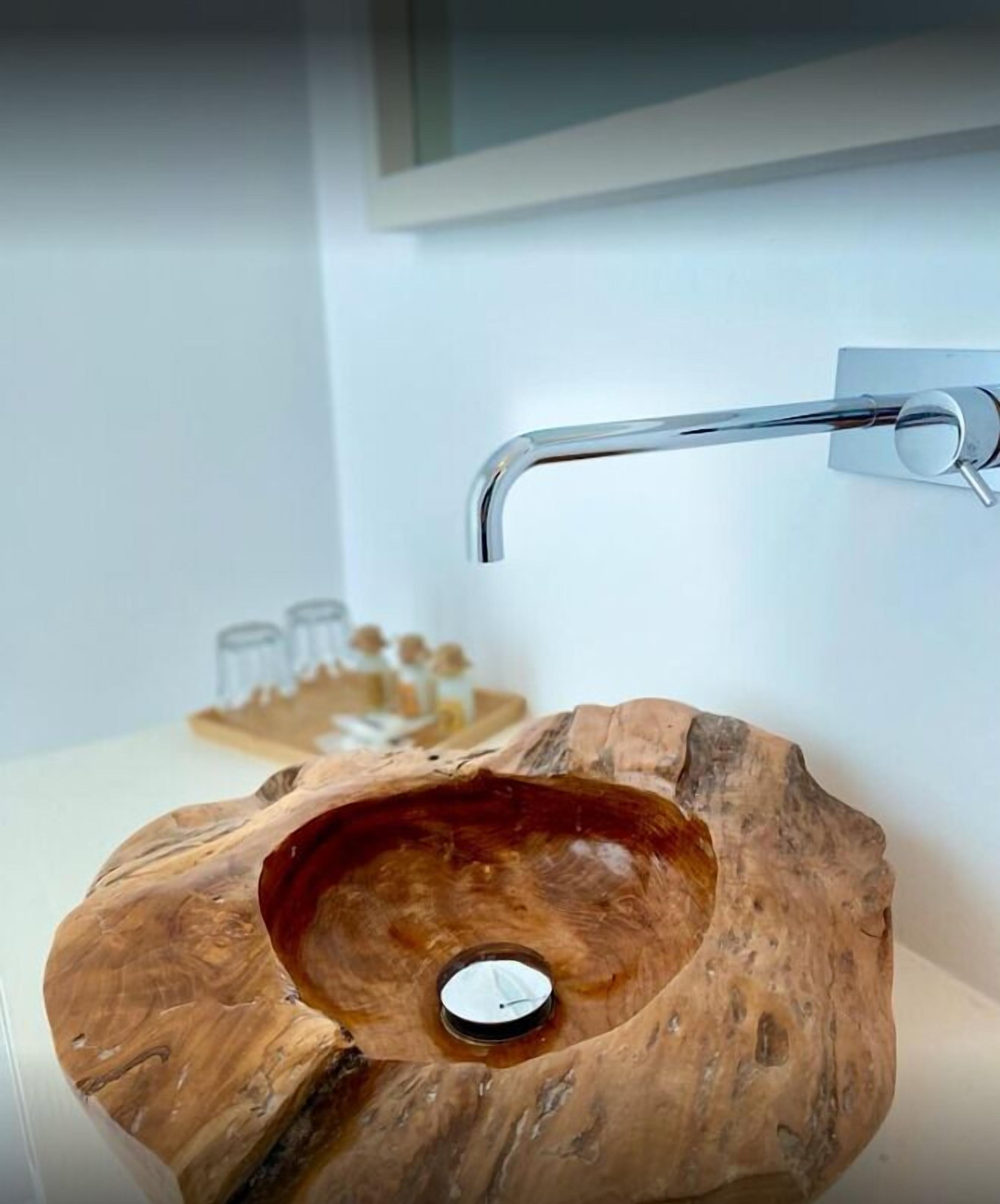 A wooden bowl sink with a faucet mounted on the wall.