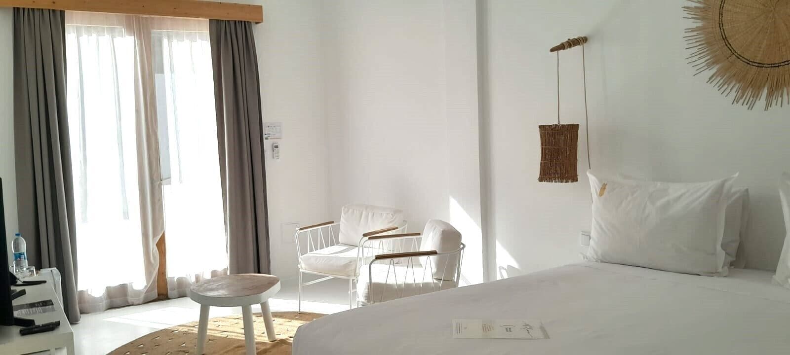 Une chambre d’hôtel avec un grand lit, une petite table, une chaise et une fenêtre avec des rideaux.