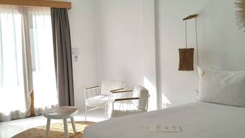 A hotel room with a large bed, a small table, a chair, and a window with curtains.