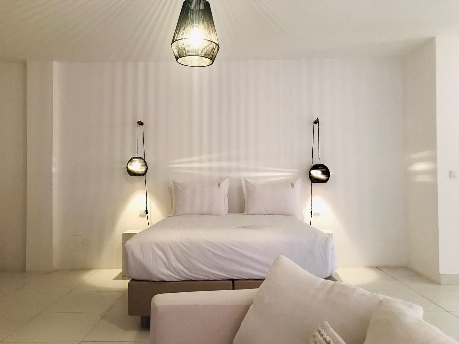 Un dormitorio minimalista con una cama grande, dos lámparas de pared y un colgante.