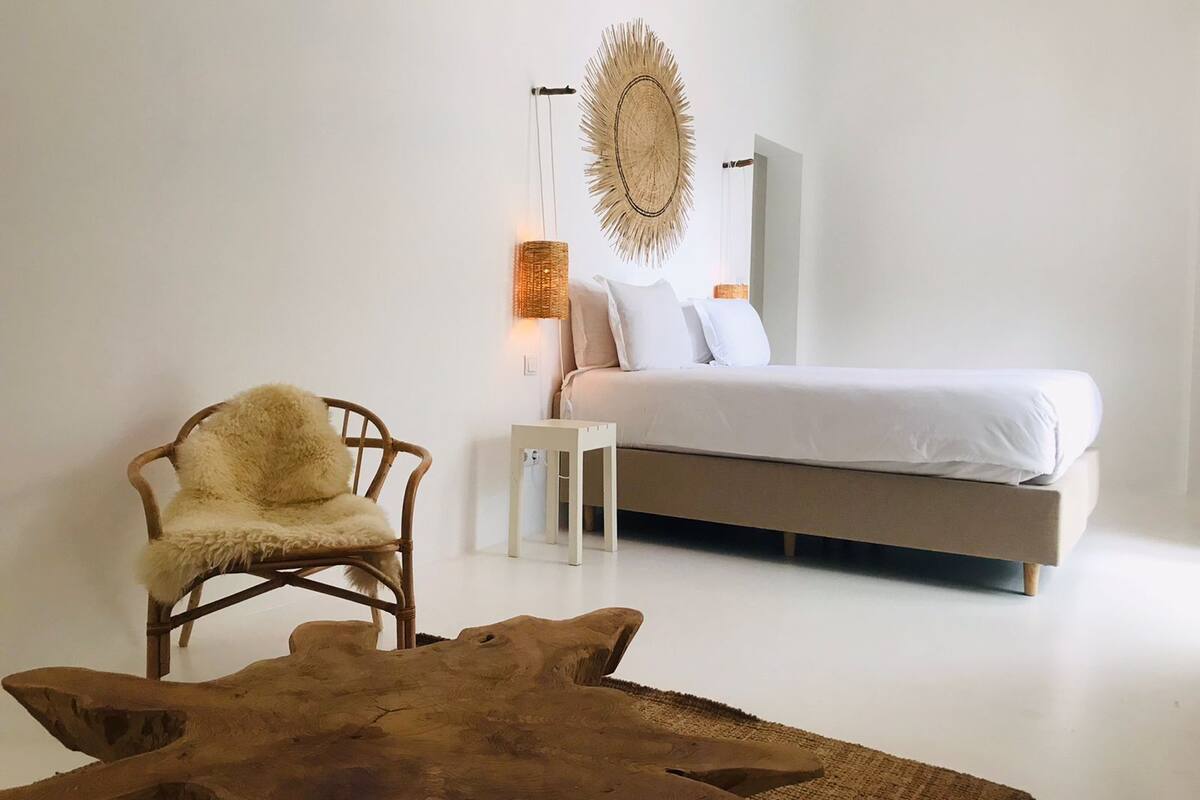 Un dormitorio minimalista con cama, una silla, una lámpara y un elemento decorativo en la pared.