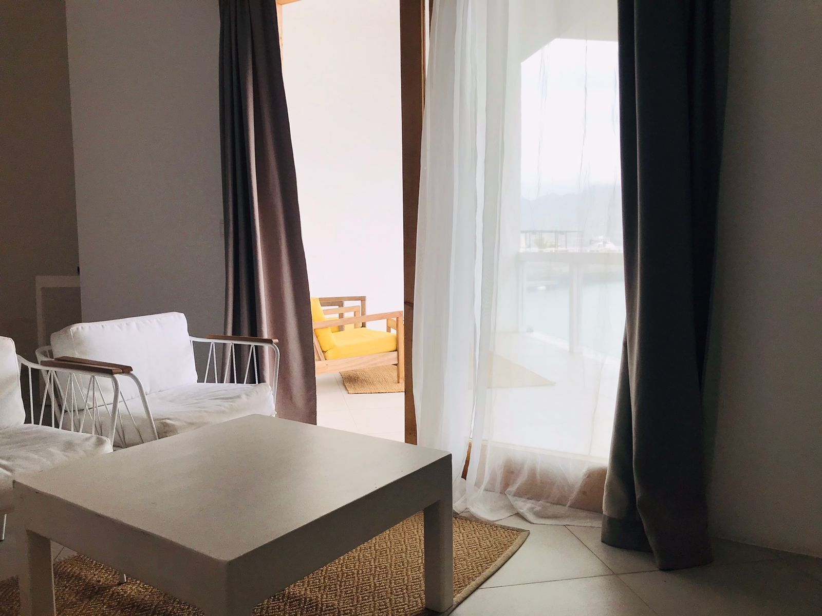 A hotel room with a bed, a small table, and a view of a balcony with a chair.