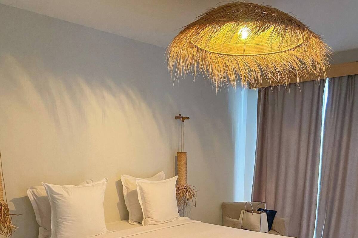Un dormitorio moderno con una cama grande, una lámpara de techo tejida, una mesita de noche y vistas al exterior.