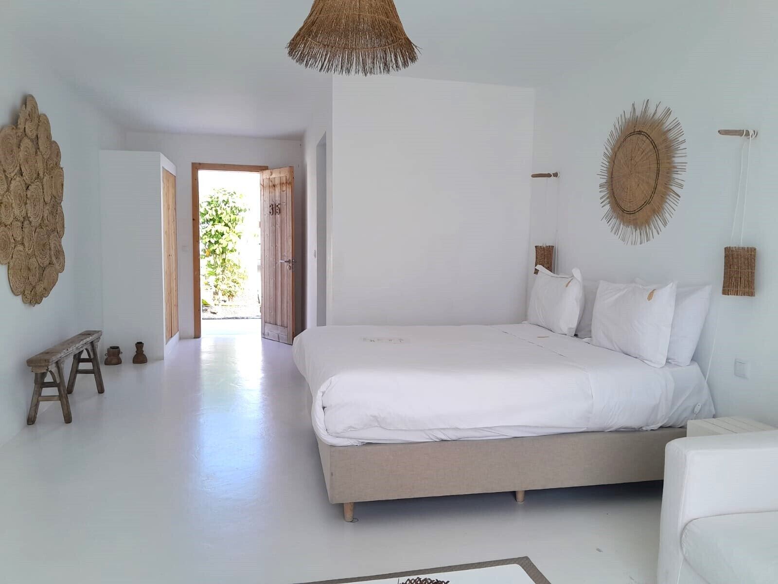 Een ruime slaapkamer met een groot bed, een houten bankje en een rustieke wandversiering.