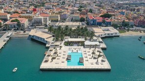 Vista aérea de una zona costera con una plaza central, una piscina y edificios circundantes.