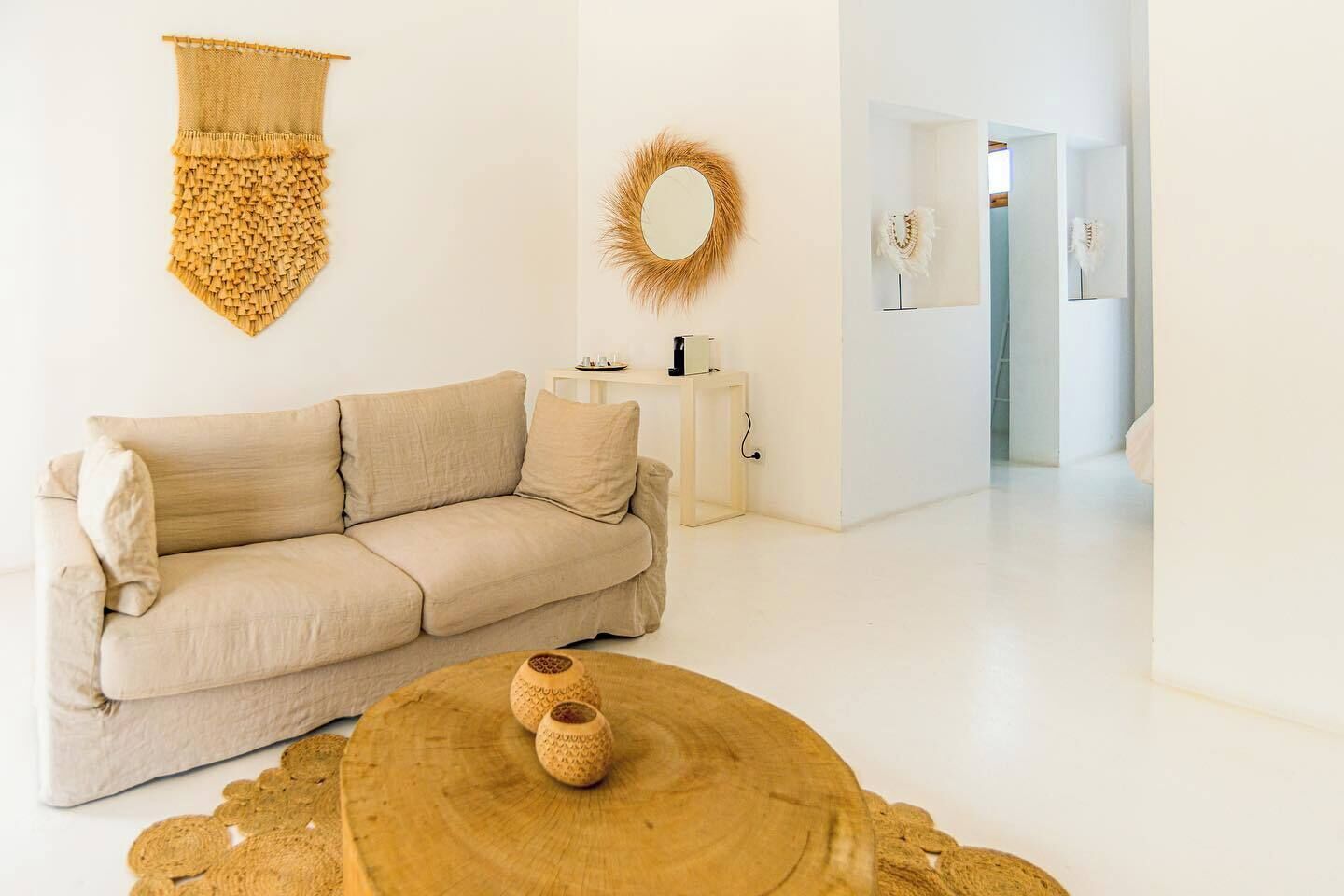 Ein modernes Wohnzimmer mit einem beigefarbenen Sofa, einem runden Holztisch und einer gewebten Wanddekoration.
