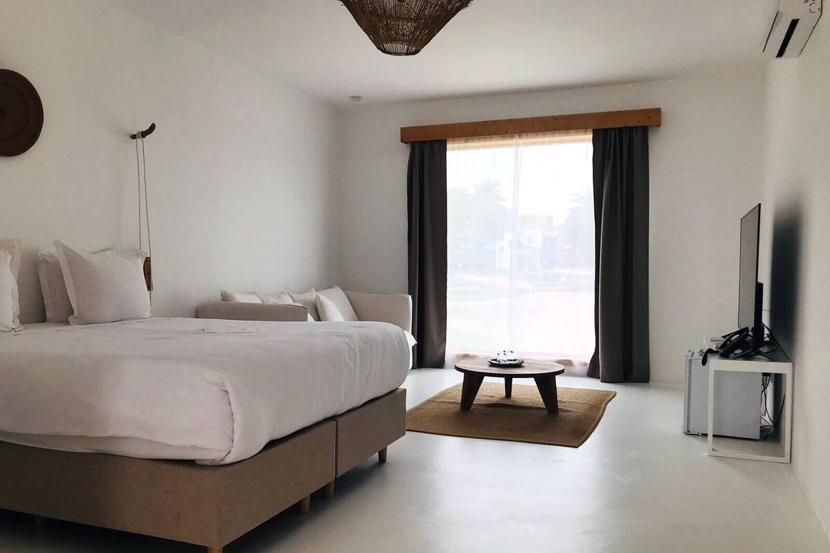 Un dormitorio moderno con una cama grande, una mesita pequeña y un televisor sobre un mueble.