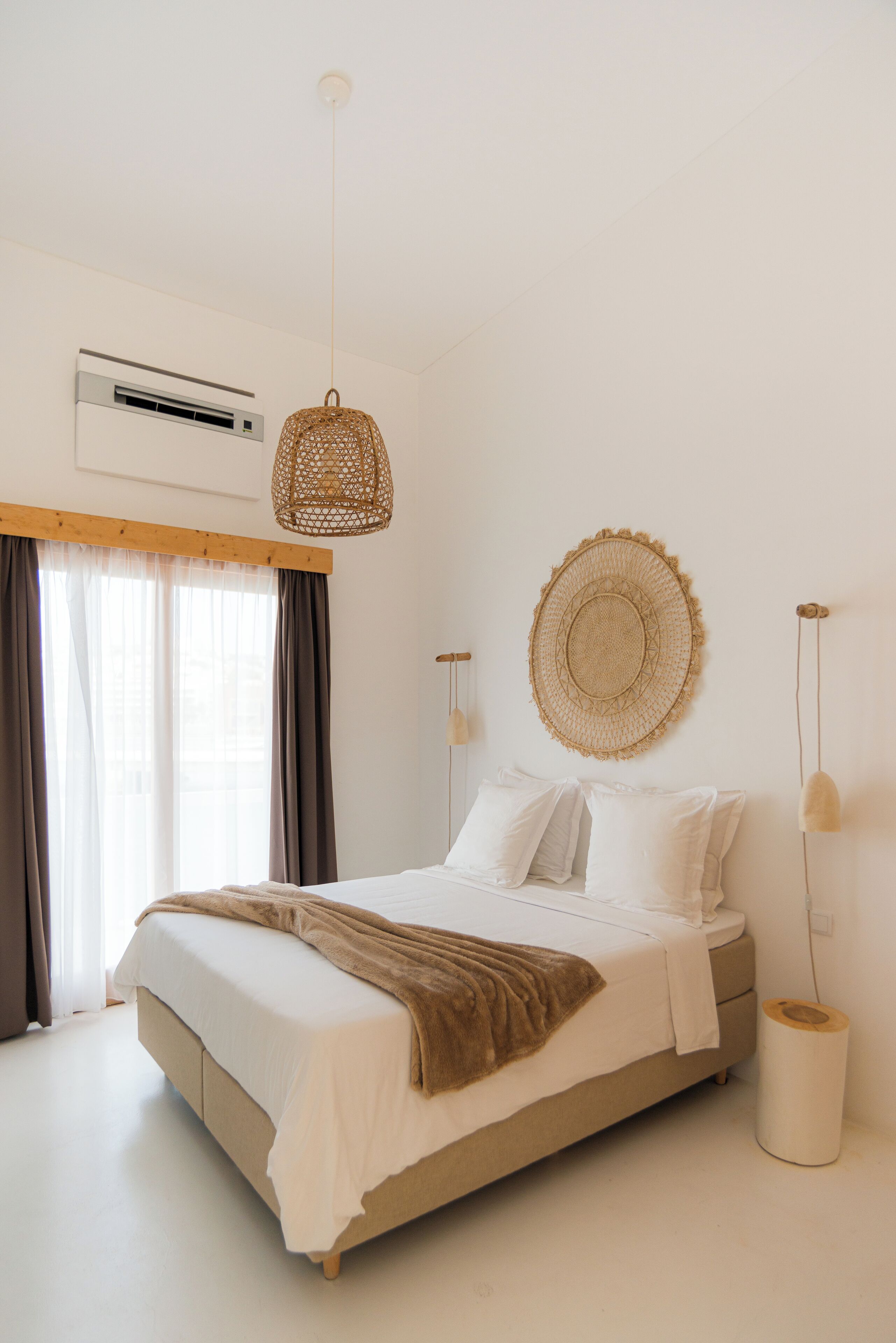 A bedroom with a bed, a hanging light, a wall-mounted air conditioner, and a window with curtains.
