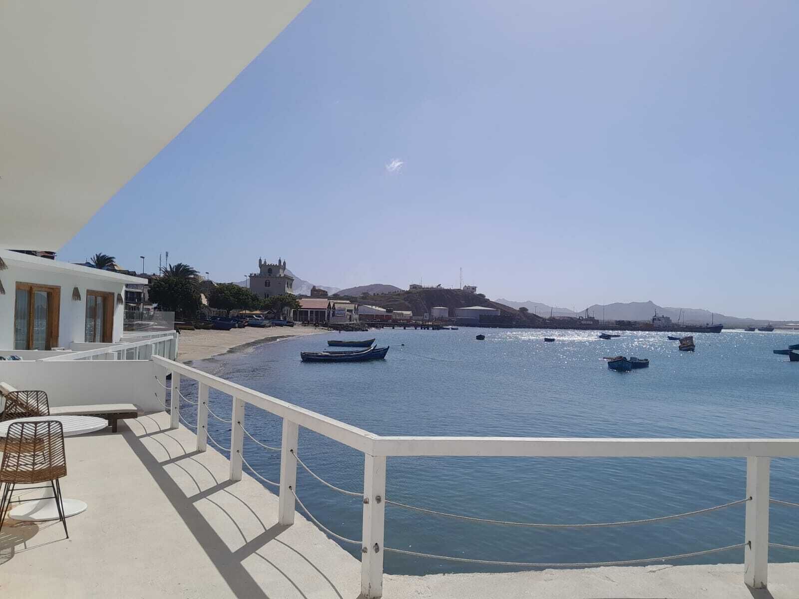Vista costera con un edificio blanco, una playa y varios barcos en el agua.