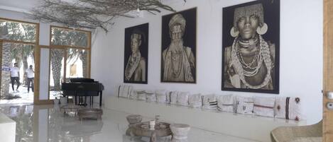 A spacious lobby with a piano, a series of framed artworks on the wall, and a display of textiles.