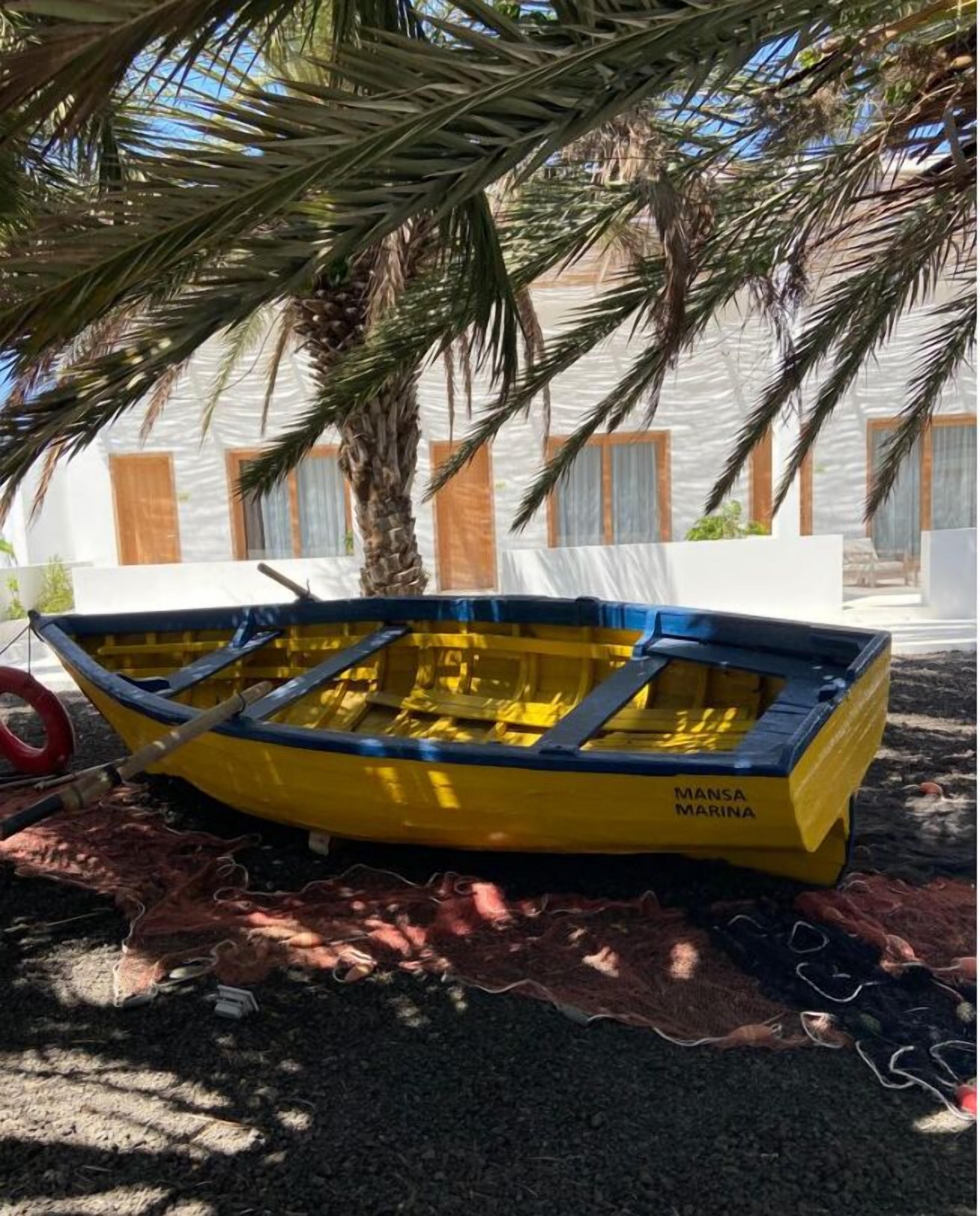 A yellow boat with "Mansa Marina" written on it, parked under a palm tree.